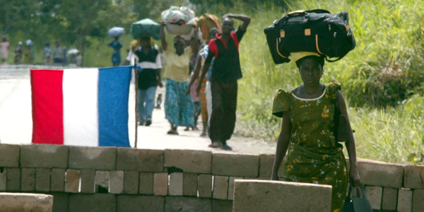 People fleeing from Bouake carry their possessions on their heads as they walk past a French army ch..