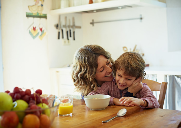 Happy mother embracing son having breakfast