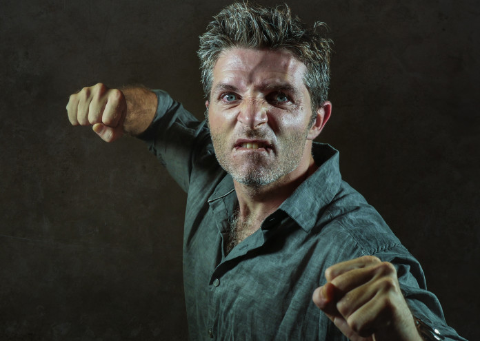  young upset and aggressive man in pub raising fist threatening throwing punch ready to fight as the violent thug troublemaker and furious wasted guy isolated on dark background 