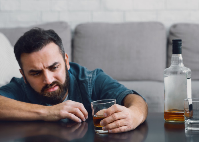  Ruined life with alcohol. Man sits at table and looks at glass in his hand 