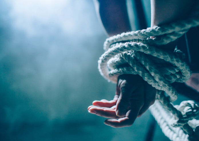  Close up and cut view of woman's hands died in a knot with a rope. One hand is up on another. Woman is tied behind her back. There is a window in dark room. Also there is a white smoke.. 